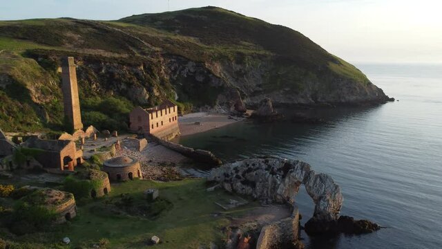 Porth Wen abandoned coastal derelict brickworks remains golden sunrise countryside bay aerial view pan left