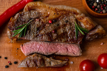 medium Rare meat cut for piece of ribeye beef meat on wooden cutting board on a wooden table stacked tomatoes garnished with hot peppers, peppercorns. Fresh food. BBQ. Macro