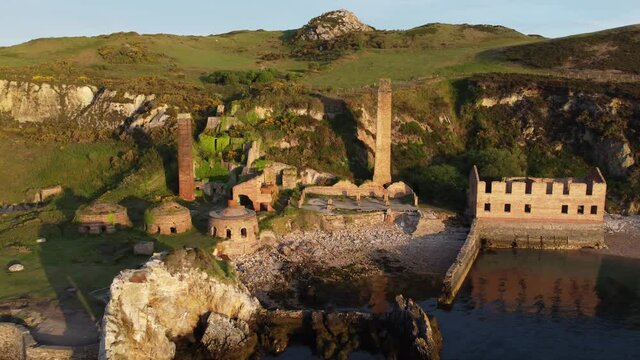 Porth Wen abandoned coastal derelict brickworks remains golden sunrise countryside bay aerial view low orbit left