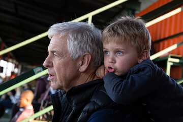 A young boy and his grandfather watching rugby from a grandstand.