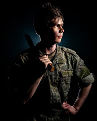 Portrait of soldier with scars and combat coloring, holding a machete in the urns on a black background