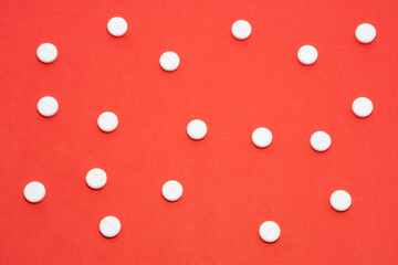Some pills placed on the red background in asymmetrical order, that generally looks like an abstract picture. The picture might be used for any articles or website about traditional medicine