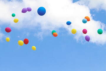 Many colorful balloons fly up into the blue sky with white clouds