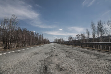 Old road in the forest against the background of the sky. Asphalt road. Beautiful nature.