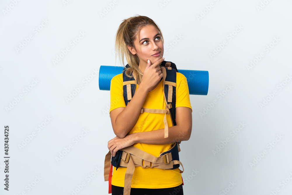 Wall mural young mountaineer woman with a big backpack isolated on white background looking up while smiling