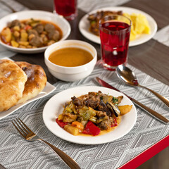 Colorful vegetable stew. Served dishes with delicious hearty food, drink and cutlery on restaurant table. Set lunch or dinner. Square format. Soft focus.