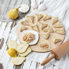 Cooking process. Sweet Dumplings with pear filling on Raw dough circles at wooden cutting board. Convenience Food concept. Ingredients and rolling pin on rustic background. Square format.