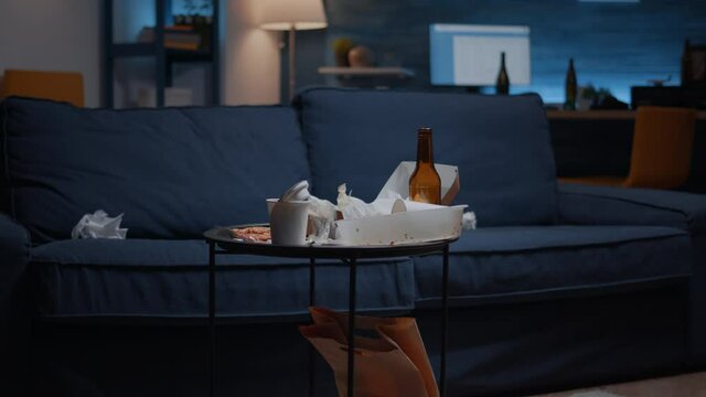 Close up of table with food and booze leftover on misery table in empty unorganized messy living room of depresive person. House apartment of alone woman with sever depresion
