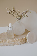 Fototapeta na wymiar Aesthetic minimalist beauty care therapy concept. Organic serum oil cosmetics bottle on stone with flowers against neutral beige background. Body skin, face treatment product composition