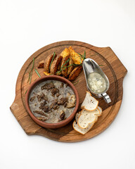 Hearty and fatty lunch. Meat broth with garnish on round wooden cutting board. Pot of rich meat soup with pork or lamb on wooden table with baked potatoes isolated on white background. Top view.