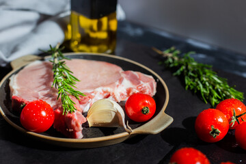 raw pork steak with cherry tomato and other ingredients such as rosemary, garlic, olive oil. copy space