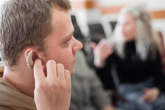 A Young Man Puts On A Hearing Aid. Portable Sound Amplifier For The Deaf And Hearing Impaired