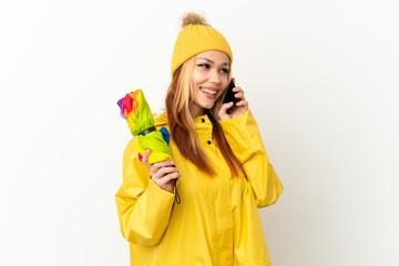 Teenager blonde girl wearing a rainproof coat over isolated white background keeping a conversation with the mobile phone