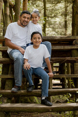 Fototapeta na wymiar Hispanic dad and sons enjoying nature in the park - young father with his children smiling at camera