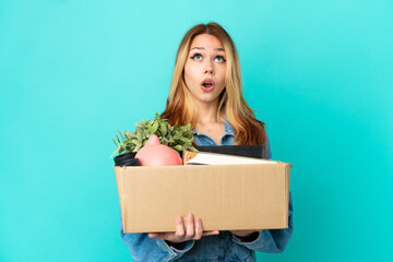 Teenager blonde girl making a move while picking up a box full of things looking up and with surprised expression