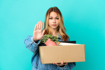 Teenager blonde girl making a move while picking up a box full of things making stop gesture
