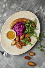 Grilled meat sausages and baked potatoes with vegetables on grey clay background