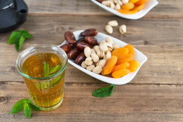 Dried fruit tray with dates, pistachios and dried apricots with tea glass on wooden bottom. Copy space.