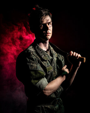 Portrait of a soldier with scars and combat coloring, holding a machete in the urns on a black background witch red smoke