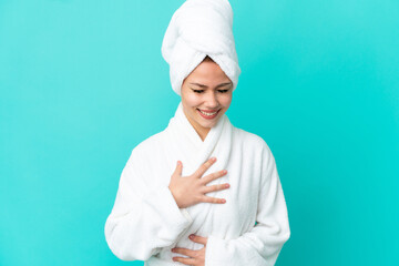 Teenager blonde girl in a bathrobe over isolated blue background smiling a lot