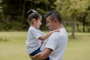 Hispanic dad hugging his little daughter in the park-father and daughter outdoors smiling face to...