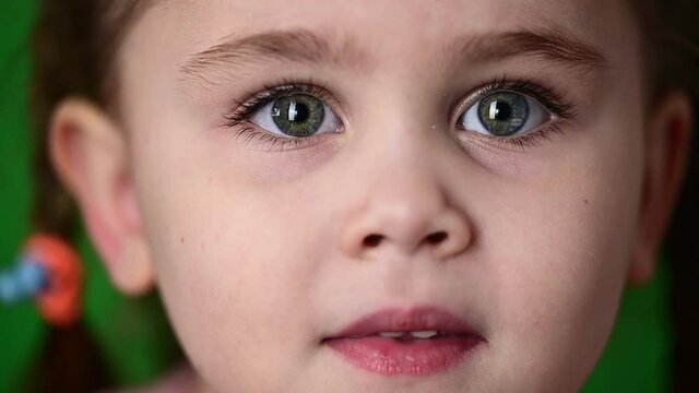Little girl blinking eyes, slow motion of a child, portrait on a green background.