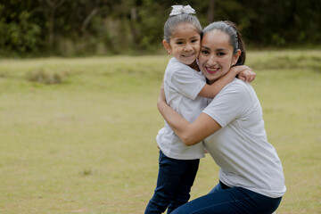 Little girl hugging her mom in the park-young hispanic mom with her daughter outdoors