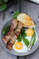 Breakfast on a plate of scrambled eggs with toasted bread, bacon and aromatic herbs