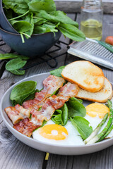 Breakfast on a plate of scrambled eggs with toasted bread, bacon and aromatic herbs