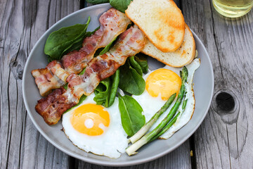 Breakfast on a plate of scrambled eggs with toasted bread, bacon and aromatic herbs