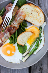 Breakfast on a plate of scrambled eggs with toasted bread, bacon and aromatic herbs