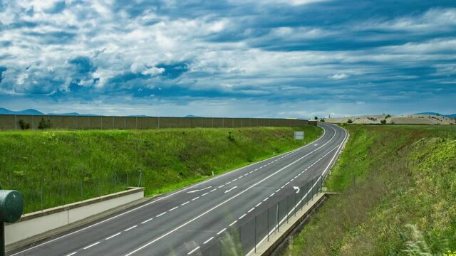 A time lapse over an asphalt-covered highway with speeding cars and rolling clouds in the sky shot in 4K