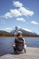 Hiker girl sitting on a wooden pier at Vermillion Lakes in Banff National Park with the snowy Rundle Mountain Range in the background