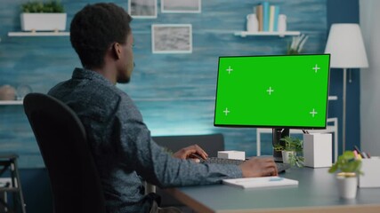 African american man using and typing on mockup computer with green screen. Computer user on isolated chroma mock up display in living room, bright house