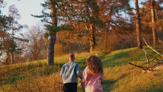 Young couple having a scamper in the morning. Guy and a girl holding hands and running together up the hill in the forest. Rear view.
