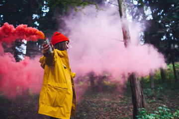 Stylish female with red smoke bomb in hand in forest
