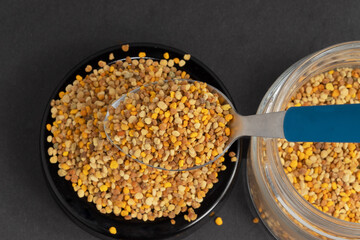 Healthy bee pollen on black background, selective focus on spoon.
