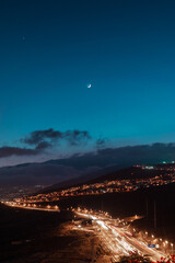  long nighttime exposure of a highway and the moon and stars over it.