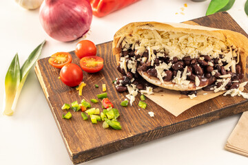 Venezuelan domino arepa with black beans and lots of grated cheese on wooden board and fresh kitchen seasonings