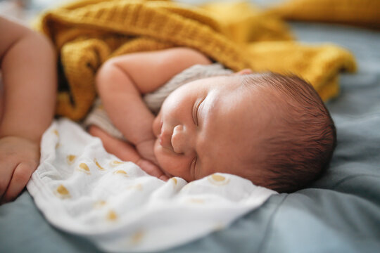 Newborn baby sleeping on a bed, top view, gray, blue and yellow color, cozy photo with a blanket