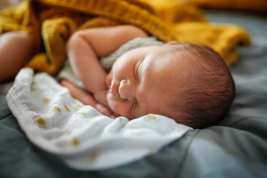 Newborn baby sleeping on a bed, top view, gray, blue and yellow color, cozy photo with a blanket