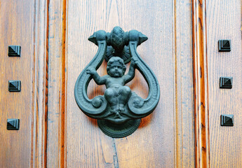 Old metal door knocker with a baby figurine on a wooden door, Florence, Italy