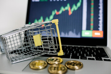 Cryptocurrencies and shopping cart or trolley on laptop with stock market graph on the background