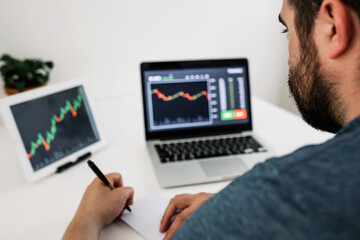 Young investor man learning stock market online through laptop. Investing and trading on crypto currencies concept