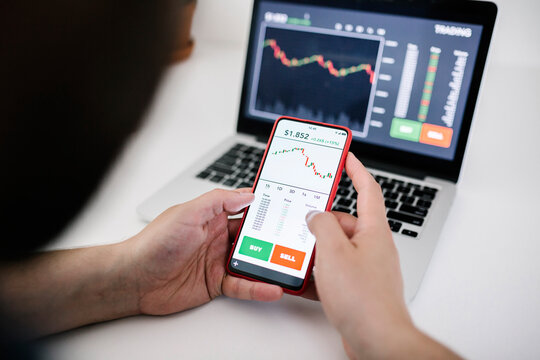 Young business man trader investor using mobile phone app to analyze cryptocurrency financial stock market - Trading online and investment concept - Focus on hand holding the phone