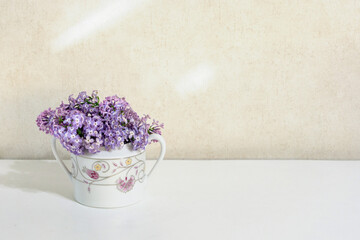 composition a bouquet of lilacs in a small porcelain vase on a white table on a beige background