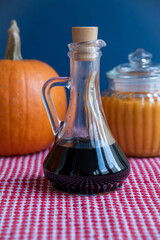 Glass bottle with pumpkin seed oil stands on red waffle fabric towel on the table. Blurred pumpkin in the background. Selective focus. Organic food theme.