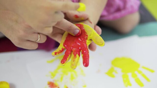 A woman smears paint on a child's palm with her finger.close-up.Slow motion.