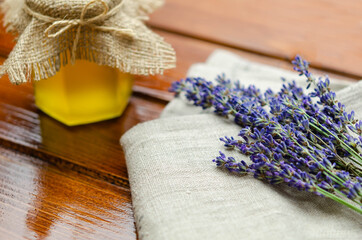 Bunch of lavender flower laying upon a fabric, next to a honey jar, on wooden background with copy space 