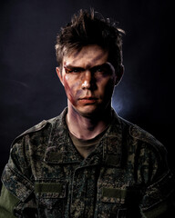 Portrait of a young soldier in uniform and combat coloring with bruises and scars on a black background